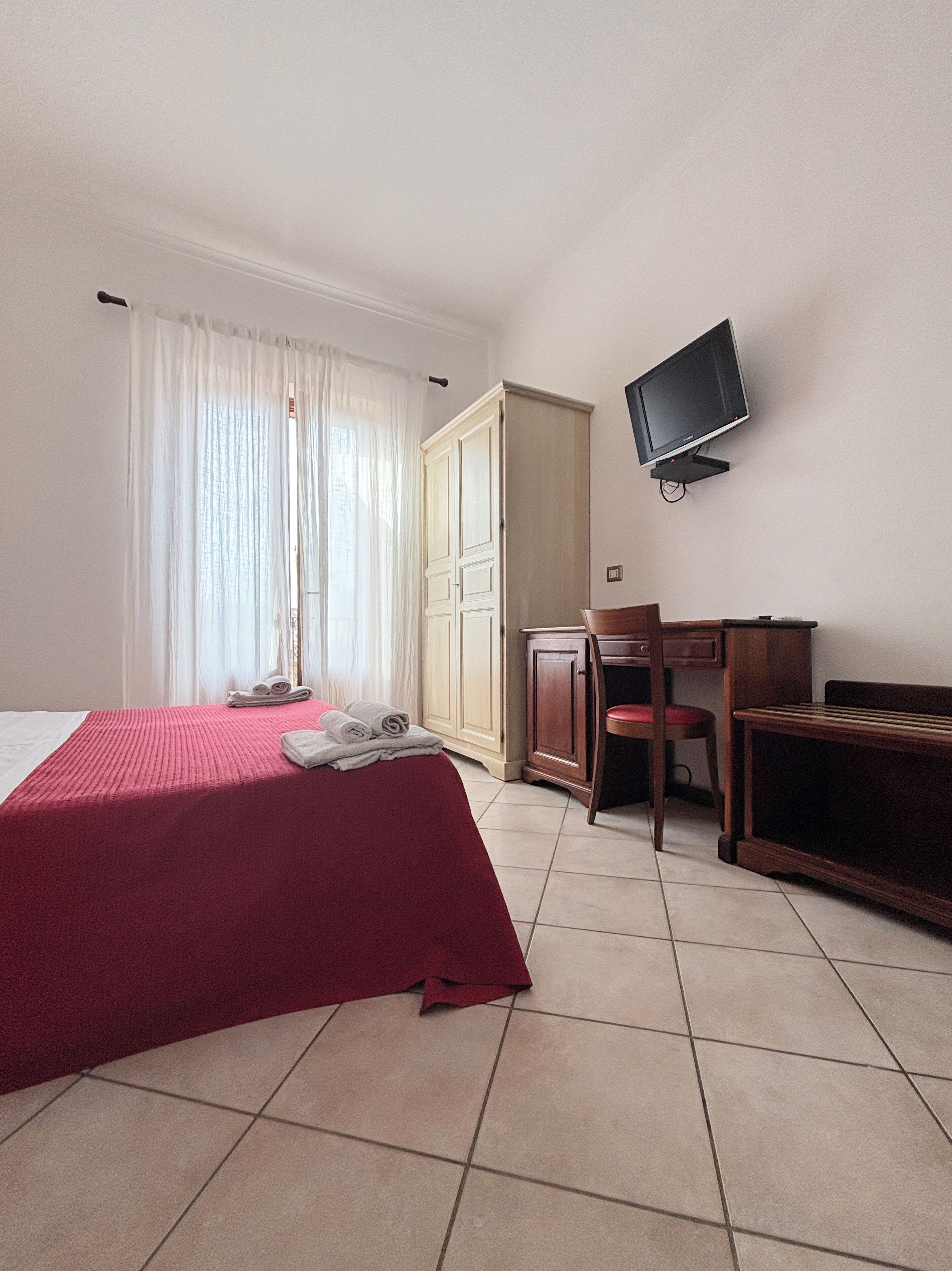 Habitación de hotel con cama, escritorio, silla, televisor y armario.