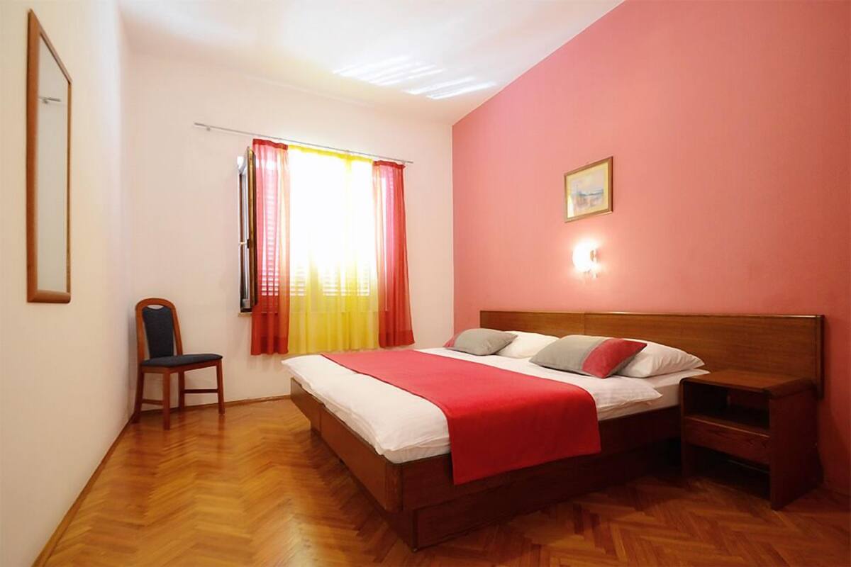 Un dormitorio con cama de madera, mesita de noche, silla y ventana con cortinas.