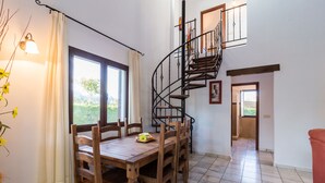 Un comedor con una mesa y sillas de madera, una escalera de caracol y vistas a zonas verdes.