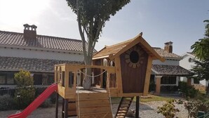 Una estructura de madera para jugar con un tobogán y un refugio parecido a un nido de pájaro.