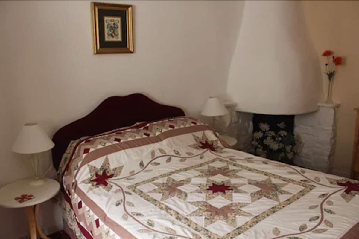 Un dormitorio con una cama, dos mesitas de noche, una mesilla auxiliar, una lámpara y un cuadro colgado en la pared.