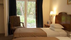 A hotel room with two beds, a chair, a lamp, and a view of greenery through the window.