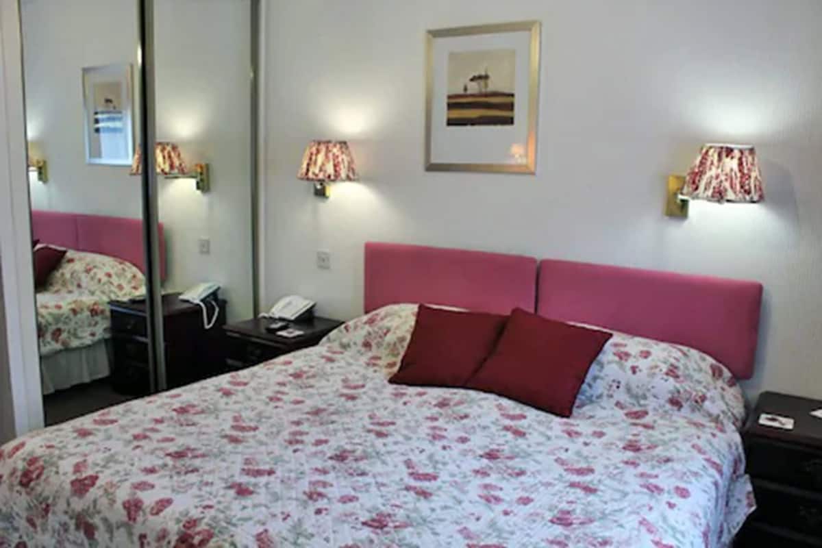 Una habitación de hotel con una cama grande, una mesita de noche, un espejo y dos lámparas de pared.