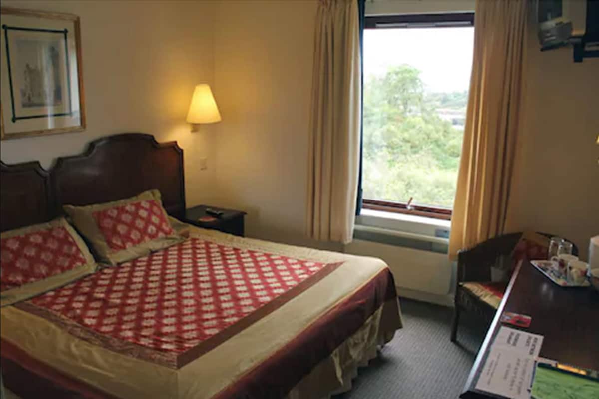 Una habitación de hotel con una cama grande, una mesita de noche, un escritorio con una silla y una ventana con cortinas.