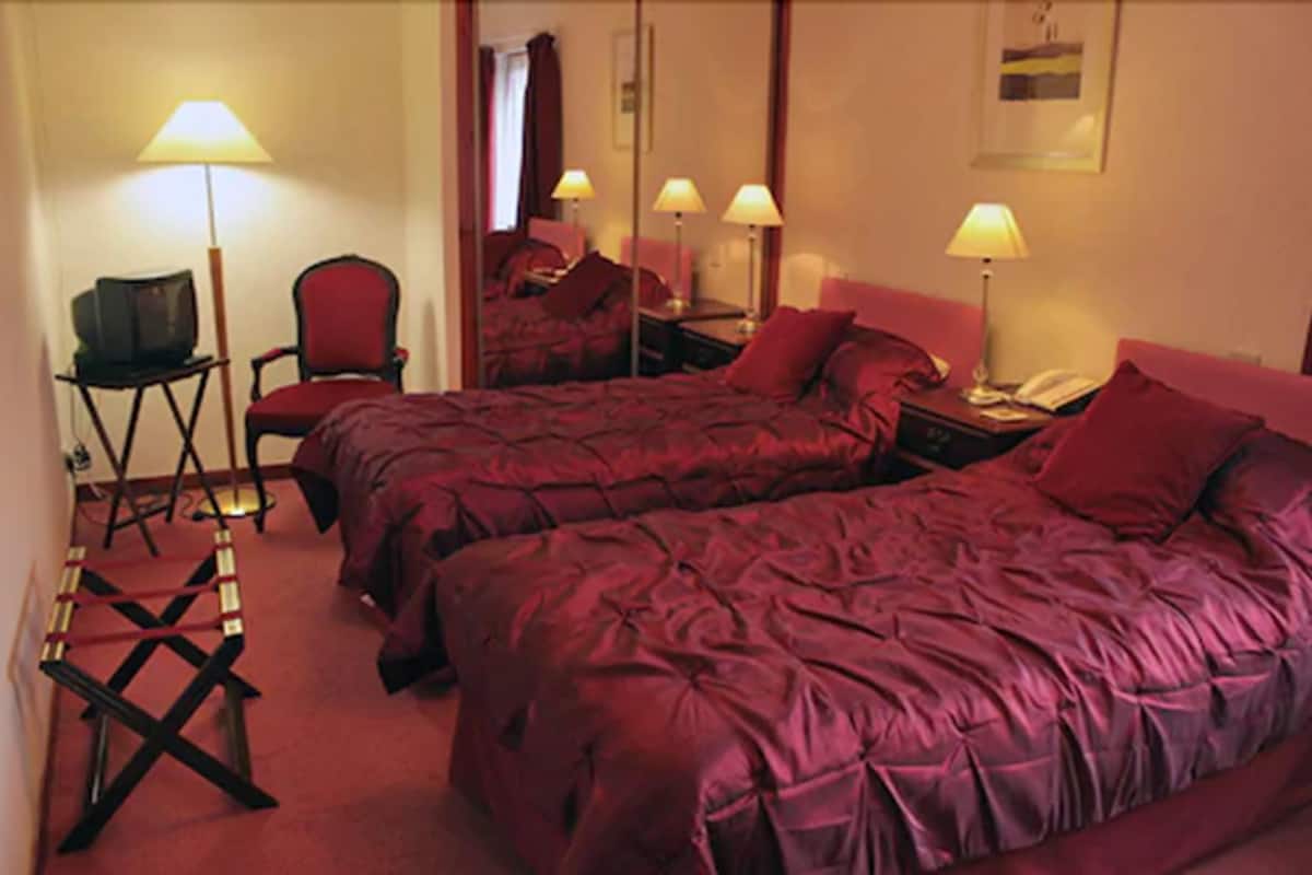 Una habitación de hotel con dos camas, un escritorio con silla, televisión y lámparas.