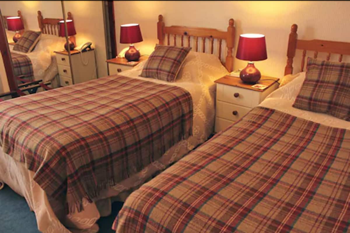 Habitación de hotel con dos camas, cada una con una colcha escocesa y una lámpara roja en la mesita de noche.