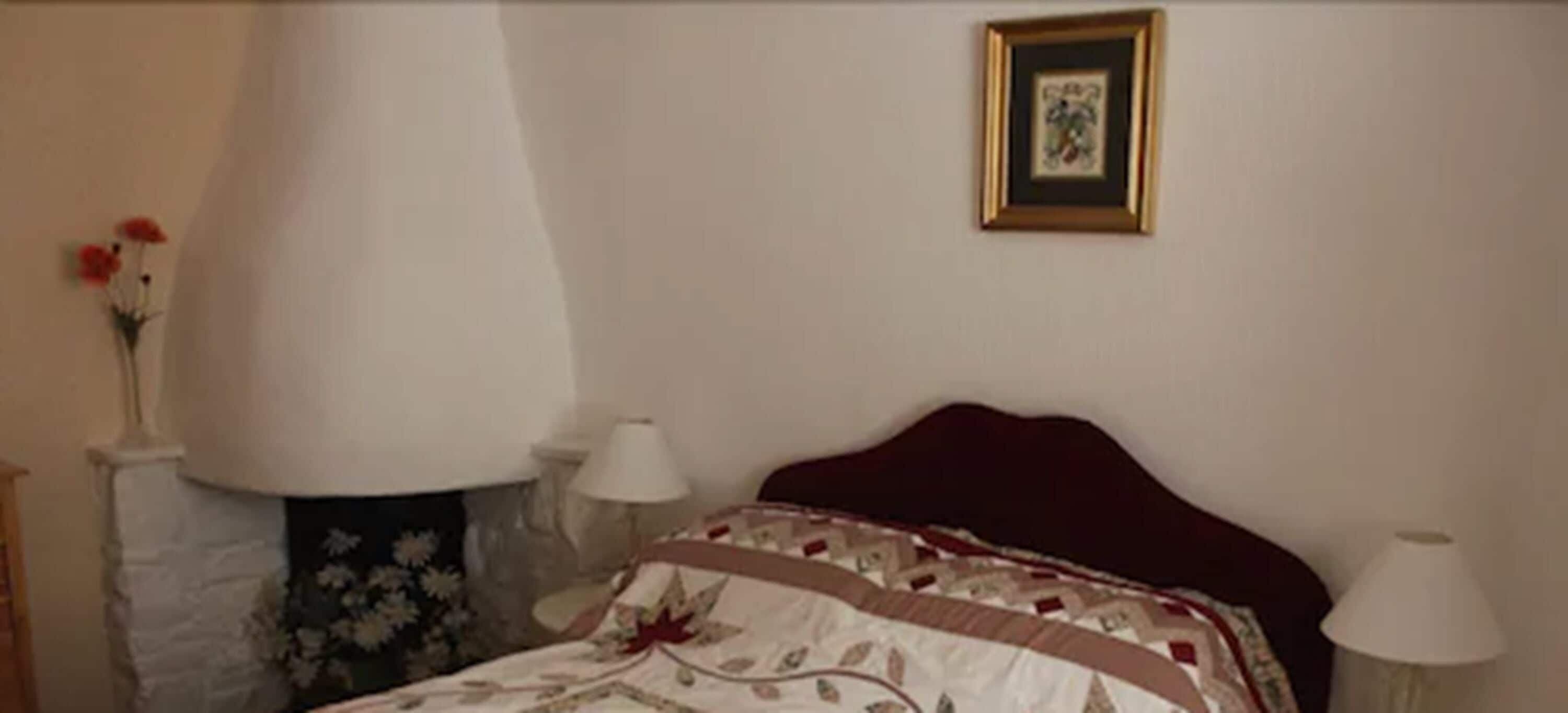 Un dormitorio con una cama, un cuadro en la pared y un florero con flores.