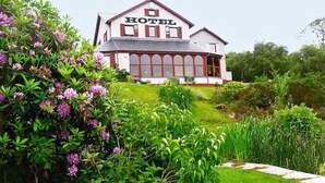 A hotel with a classic architectural style, featuring a prominent 'HOTEL' sign above the entrance, a red and white facade, and a well-maintained garden with various plants and shrubs.