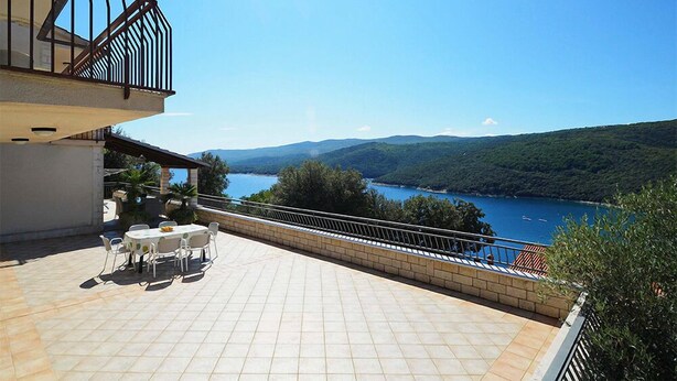 Una terraza con mesa y sillas que da a un lago y colinas.