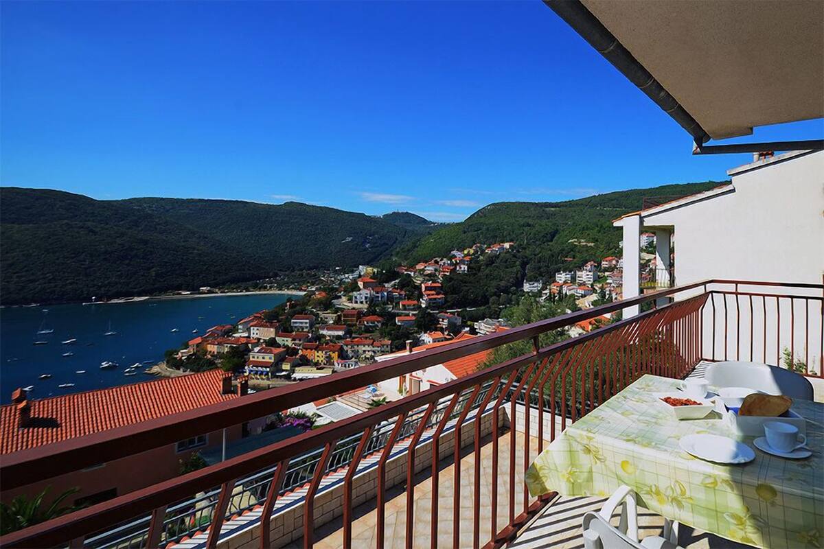 Ein Balkon mit Frühstückstisch, der auf eine Küstenstadt mit Häusern und Booten blickt.