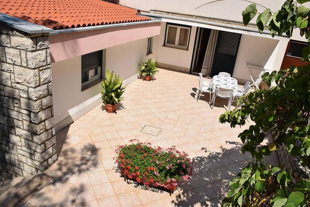 Ein Innenhof mit Fliesenboden, Steinmauer, kleinem Garten und einer Sitzgelegenheit mit Stühlen und Tischen.