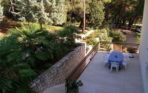 A balcony with a stone wall, outdoor furniture, and surrounding greenery.