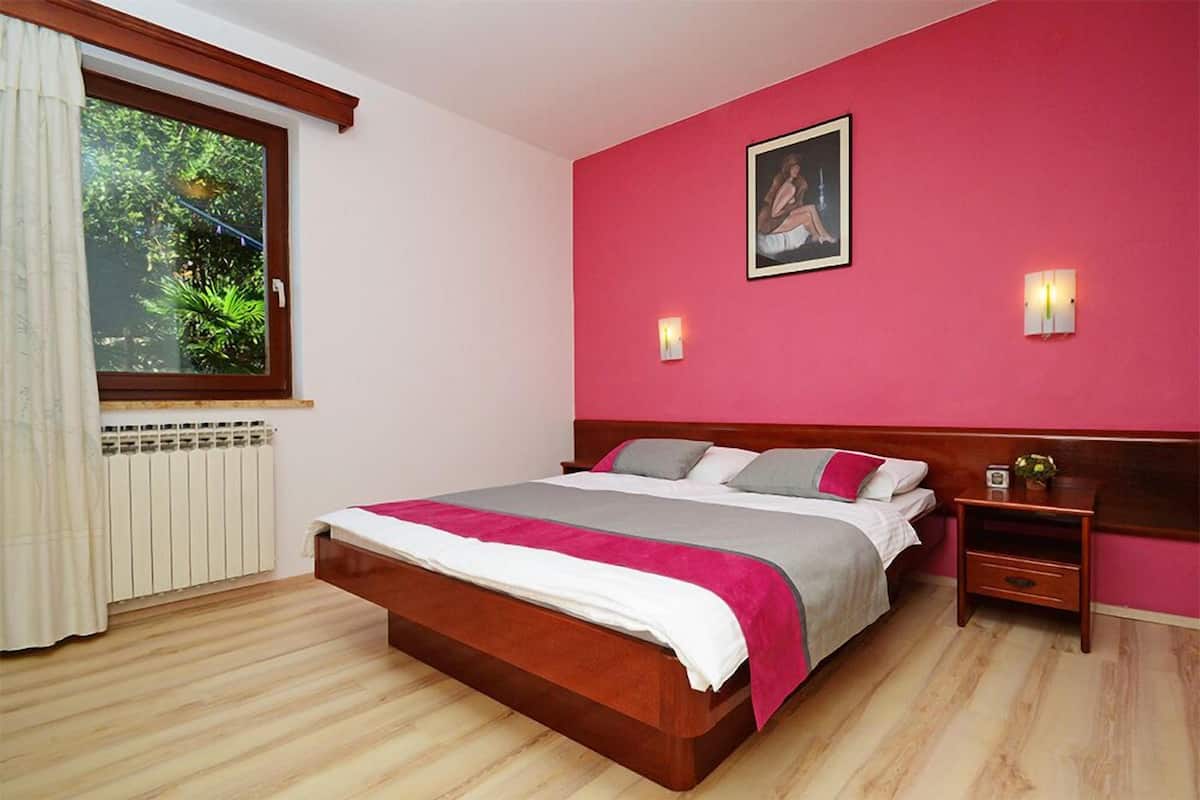 Ein Schlafzimmer mit einem hölzernen Bett, einem Nachttisch, einem Fenster mit Vorhängen und einem an der Wand hängenden Bild.