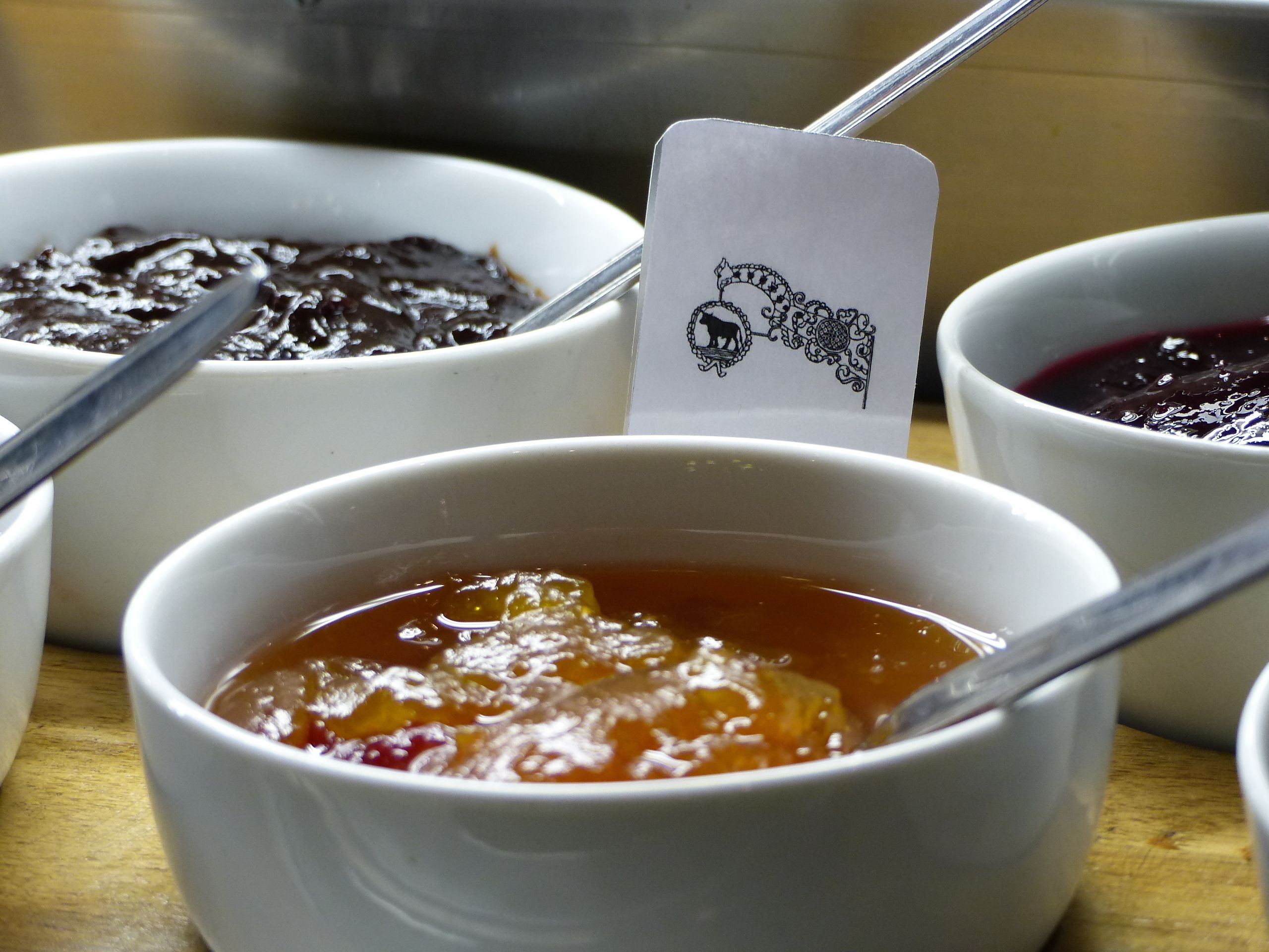 Four bowls of different sauces with spoons in them, placed on a wooden table.