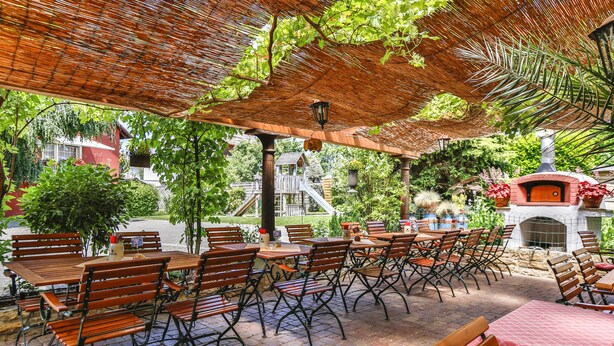 Un patio al aire libre con mesas y sillas de madera, suelo de ladrillo y un horno de ladrillo.