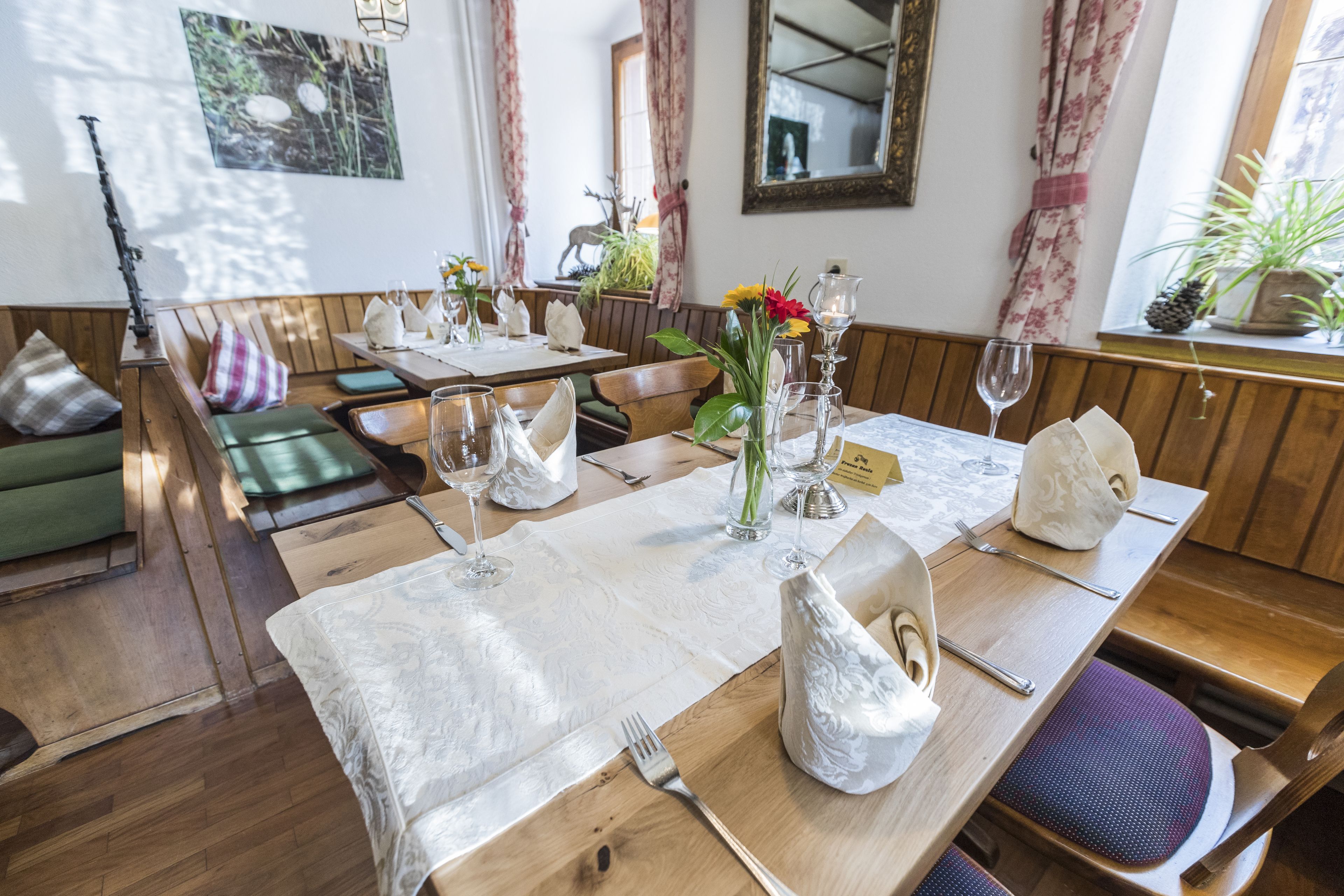 Un comedor con mesas de madera, manteles blancos y bancos acolchados de color verde.