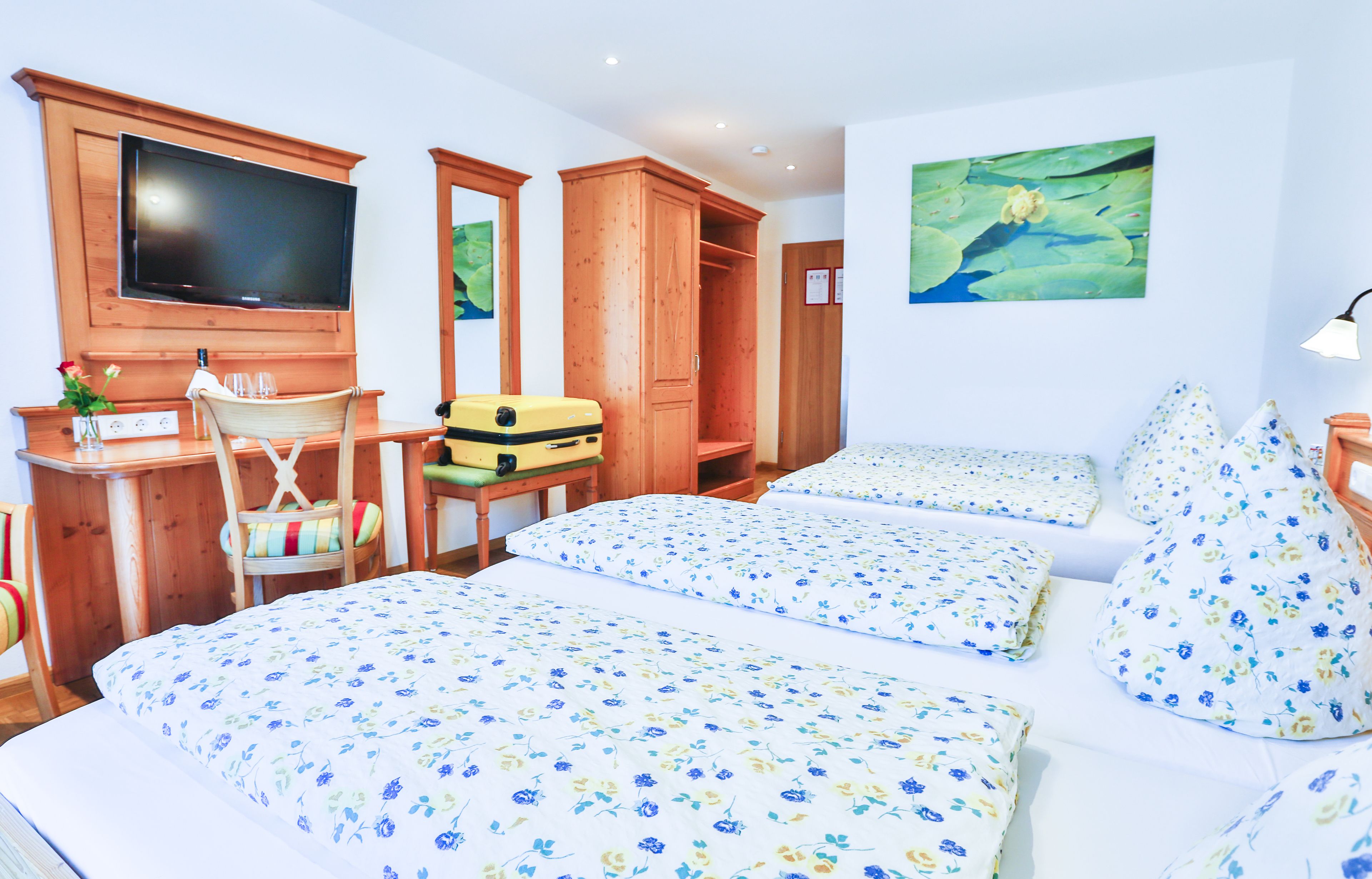 A hotel room with two beds, a TV, a wooden wardrobe, a desk with a chair, and a painting of a pond.