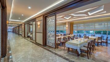 A spacious dining area with multiple tables and chairs, a decorative partition, and a view of the outdoors through large windows.