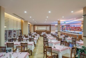 Un restaurante espacioso con varias mesas y sillas, una pared decorativa en el centro y una vitrina con postres.