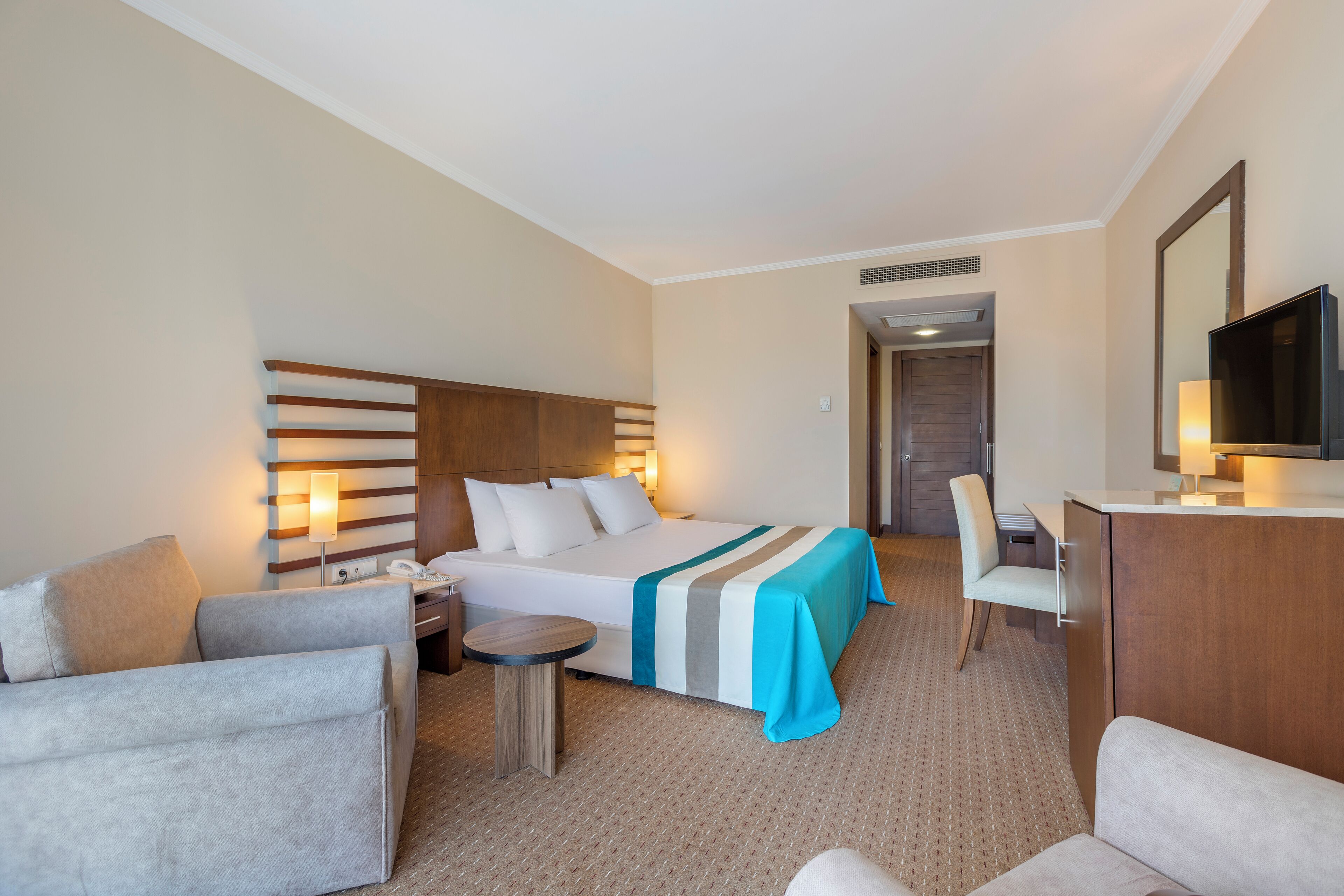 Une chambre d’hôtel avec un lit, deux fauteuils, un bureau et une télévision.