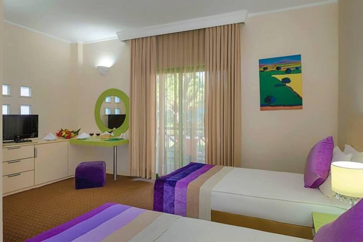 A hotel room with two beds, a desk with a mirror, a television, and a painting on the wall.