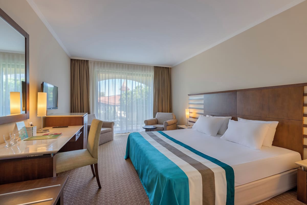 A hotel room with a large bed, a desk with a chair, a sofa, and a TV.