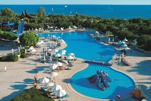 A large outdoor swimming pool with a water slide, surrounded by lounge chairs and umbrellas. - Green Max Hotel (Serik)