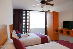 Habitación de hotel con dos camas, una televisión y puerta corredera a un balcón.