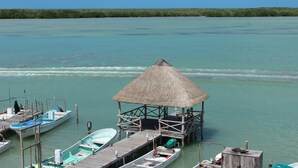 Een steiger met een rieten dak, boten afgemeerd, en kalm turquoise water.