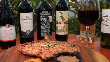 Una mesa de madera con un filete a la parrilla, patatas asadas y una copa de vino tinto.