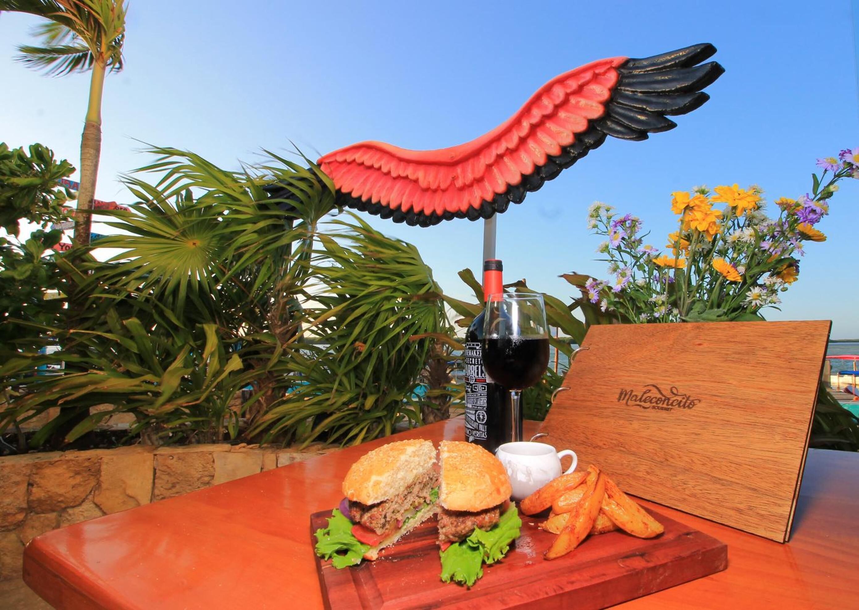 Une table avec un sandwich, des frites, une boisson et une planche en bois portant l’inscription « Malecocos ».