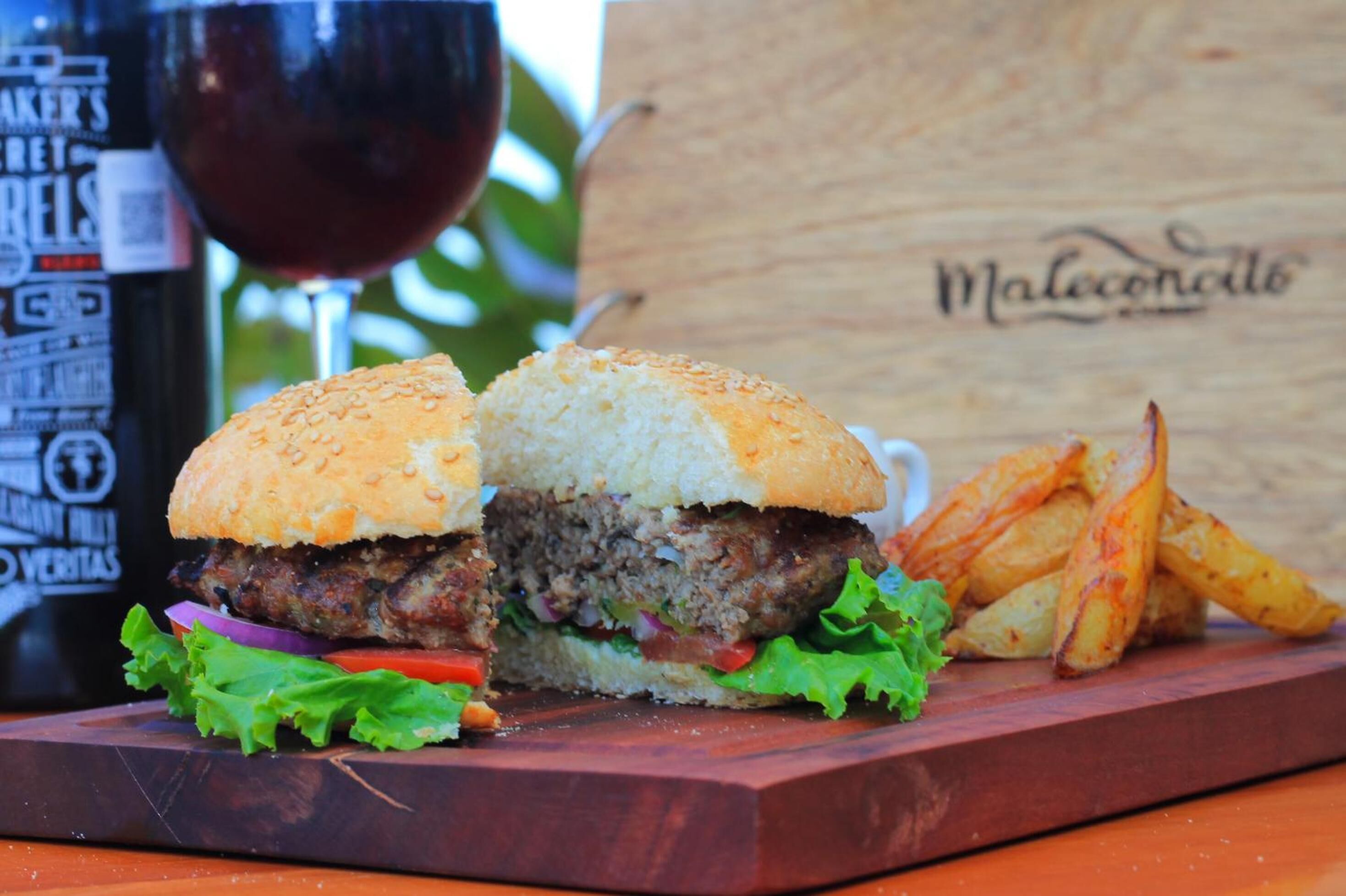 Una hamburguesa con papas fritas y una copa de vino tinto sobre una tabla de madera.