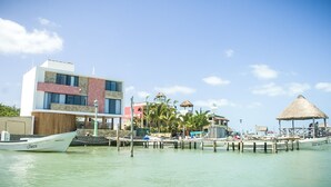 Een hotel aan het water met een modern gebouw, een steiger met boten en een constructie met rieten dak.