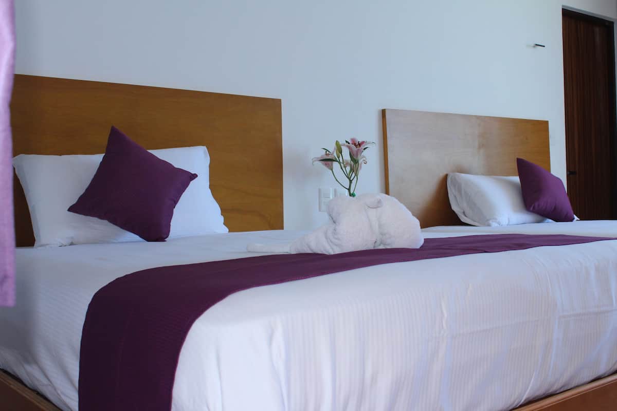 Una cama bien hecha con ropa de cama blanca y morada, un cabecero de madera y una manta morada.