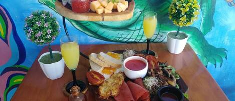 A wooden table with a variety of food items and drinks, including a plate of sliced fruits, a bowl of soup, and a glass of juice.