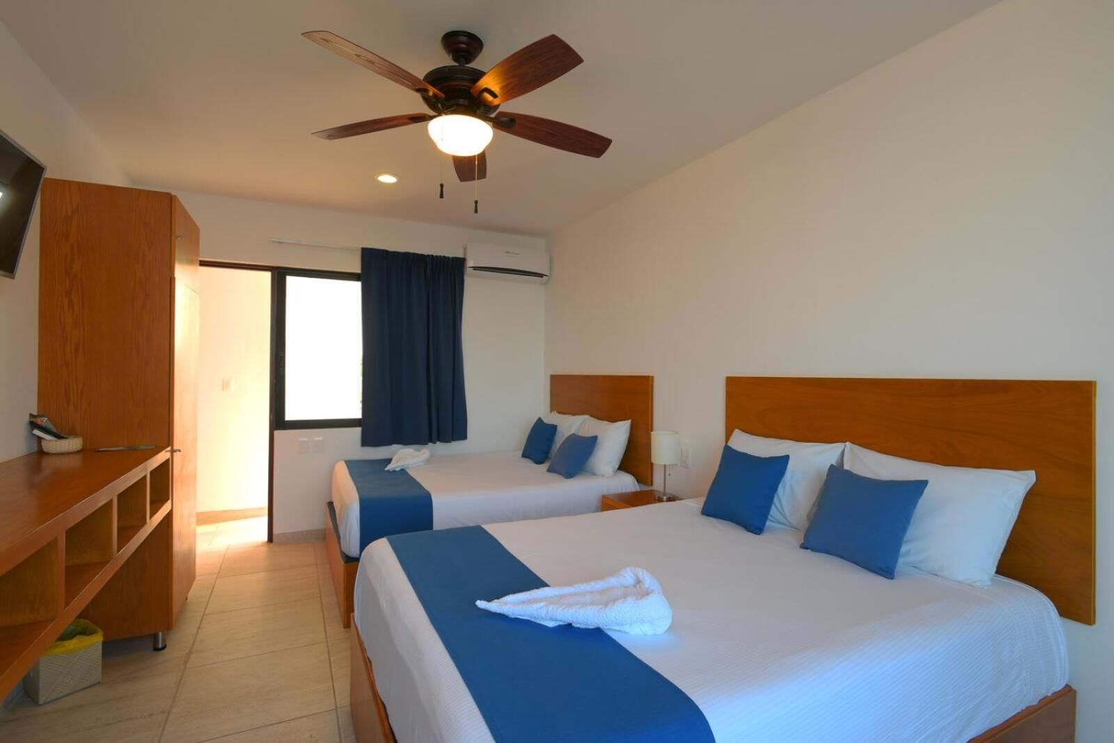 A hotel room with two beds, a ceiling fan, and a desk.