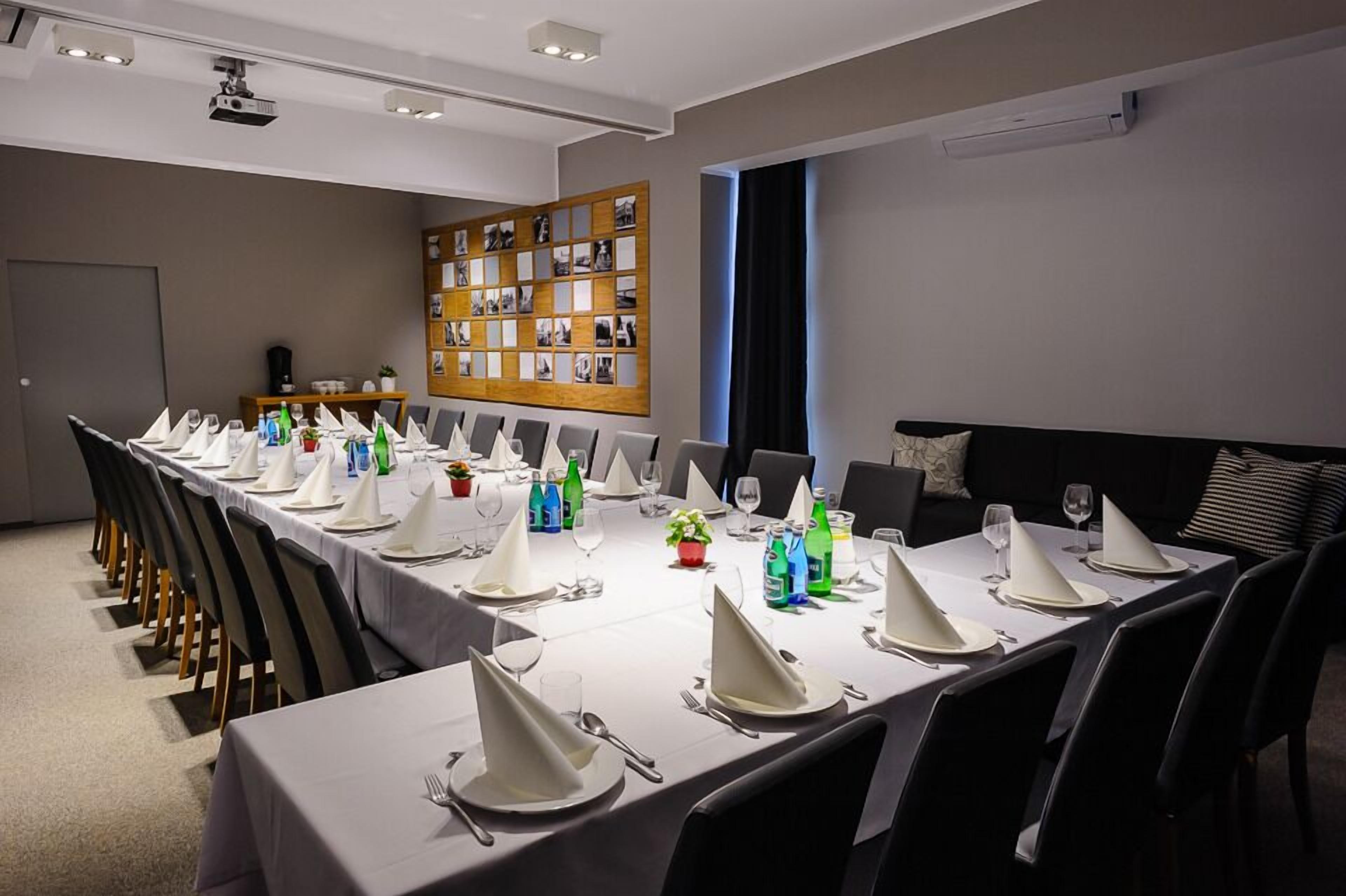 A conference room with a long table set for a meeting, equipped with chairs, tables, and a projector.