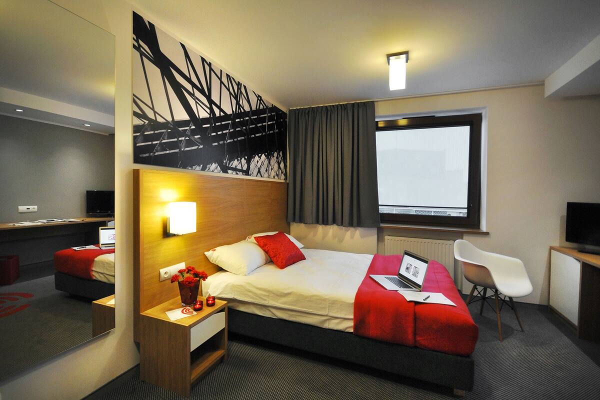 A modern hotel room with a large bed, a desk, a chair, and a TV.