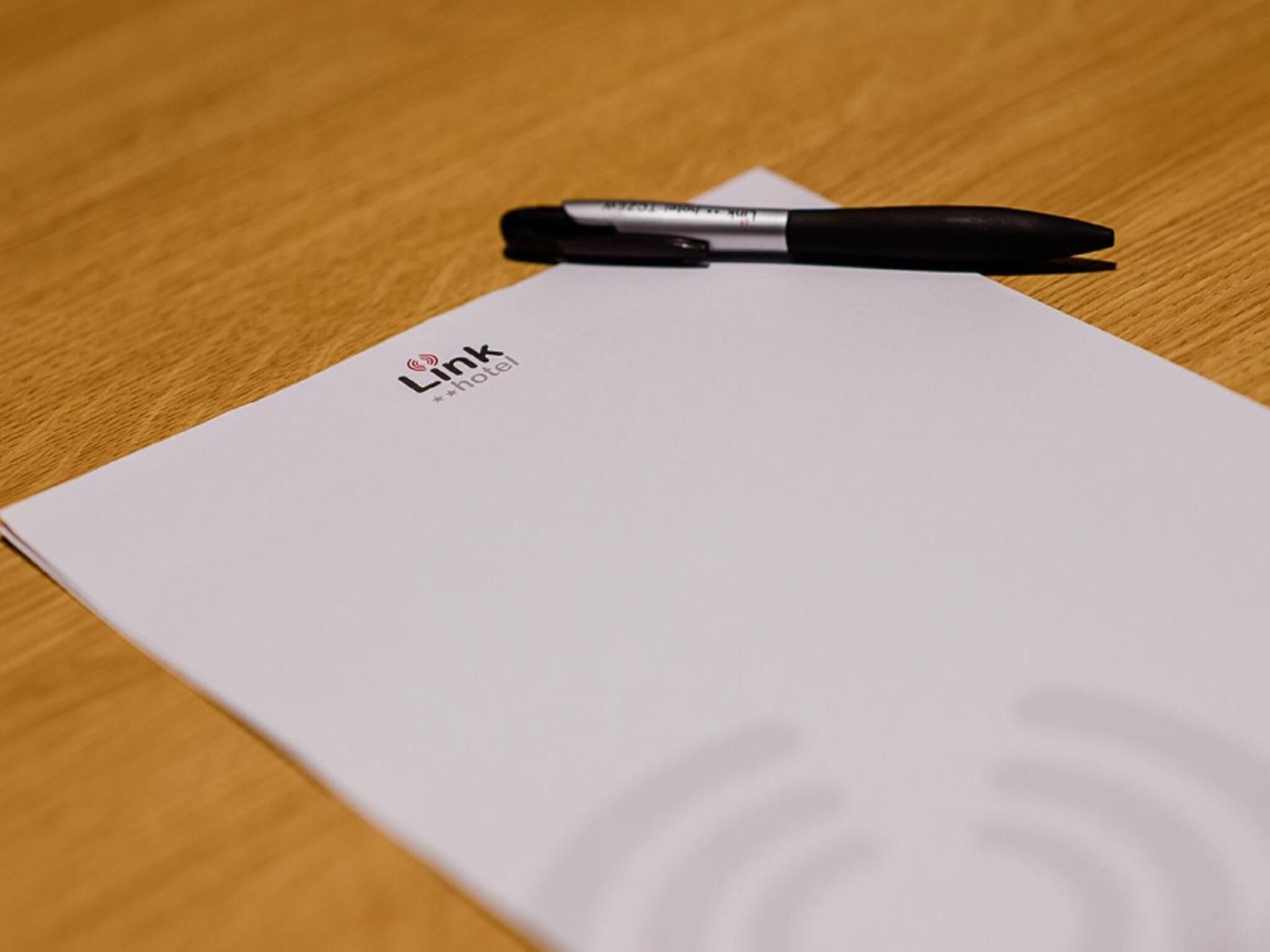 A white hotel brochure with the logo "Link hotel" and a black pen on top.