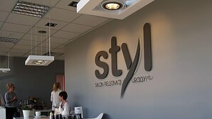 A salon interior with a reception desk, a large 'styl' sign, and a few people in the background.
