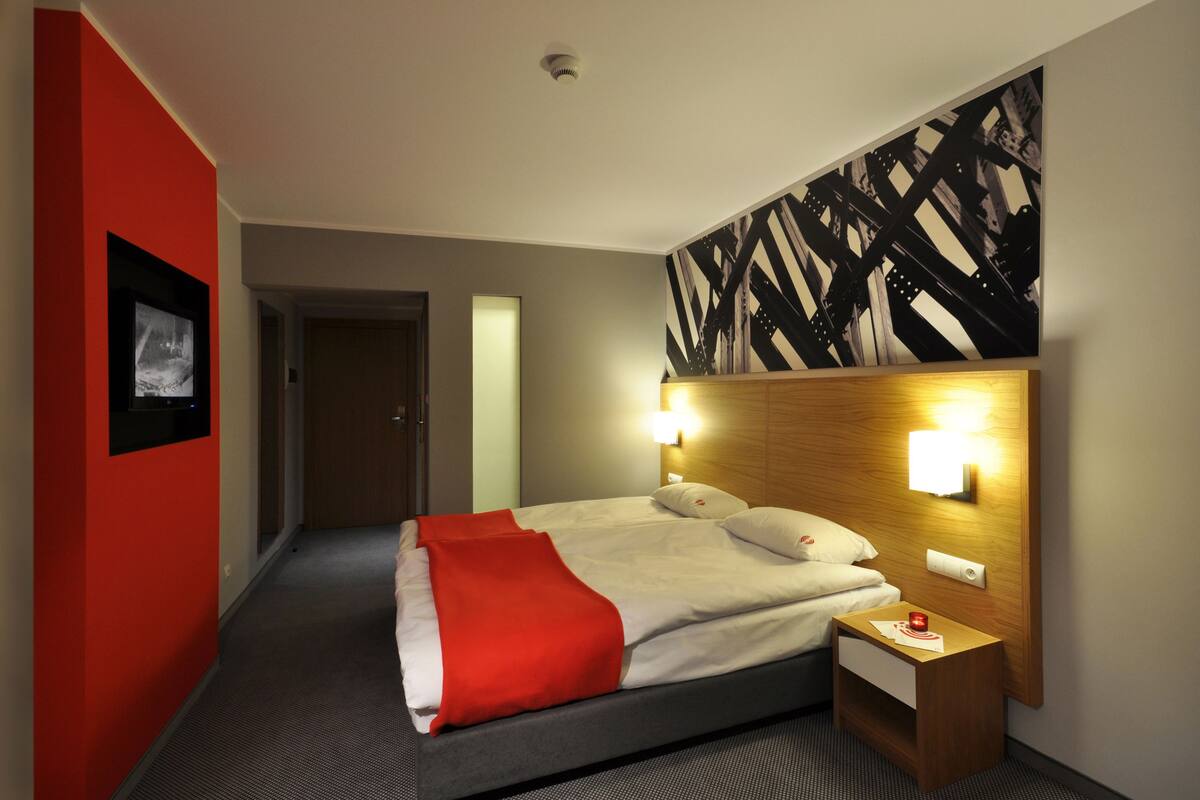 A hotel room with a bed, bedside table, and a wall-mounted artwork.