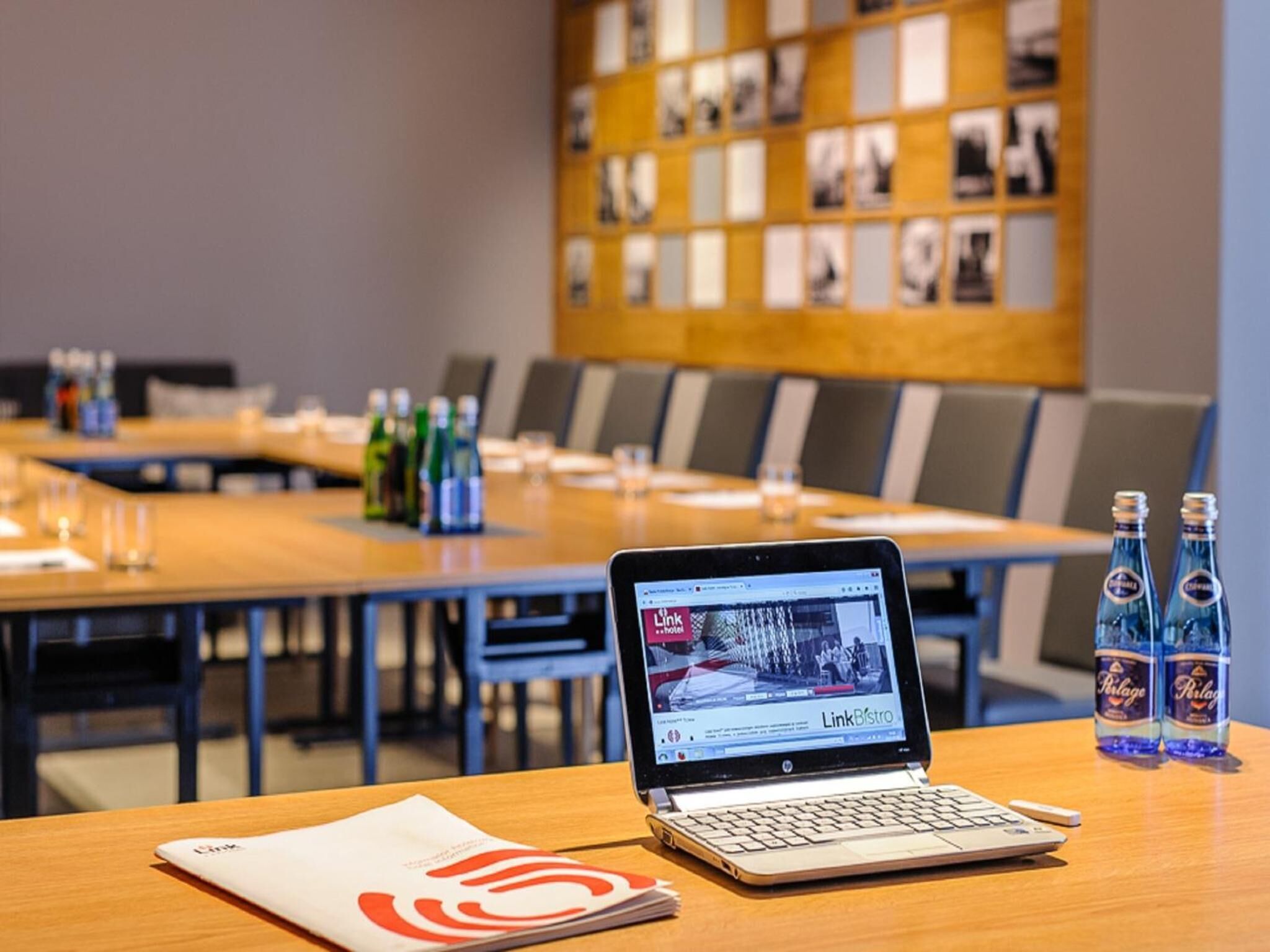 A conference room with a laptop on a table, a bottle of Pilsner beer, and a Link hotel brochure.