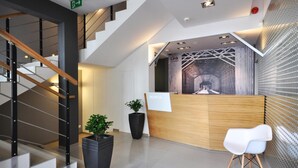 A modern hotel reception area with a wooden reception desk, a white chair, and a staircase with metal railings.