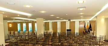 A conference room with rows of chairs, a podium, flags, and recessed lighting.