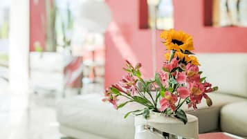 A modern living room with a glass coffee table, a vase with flowers, and a red wall.