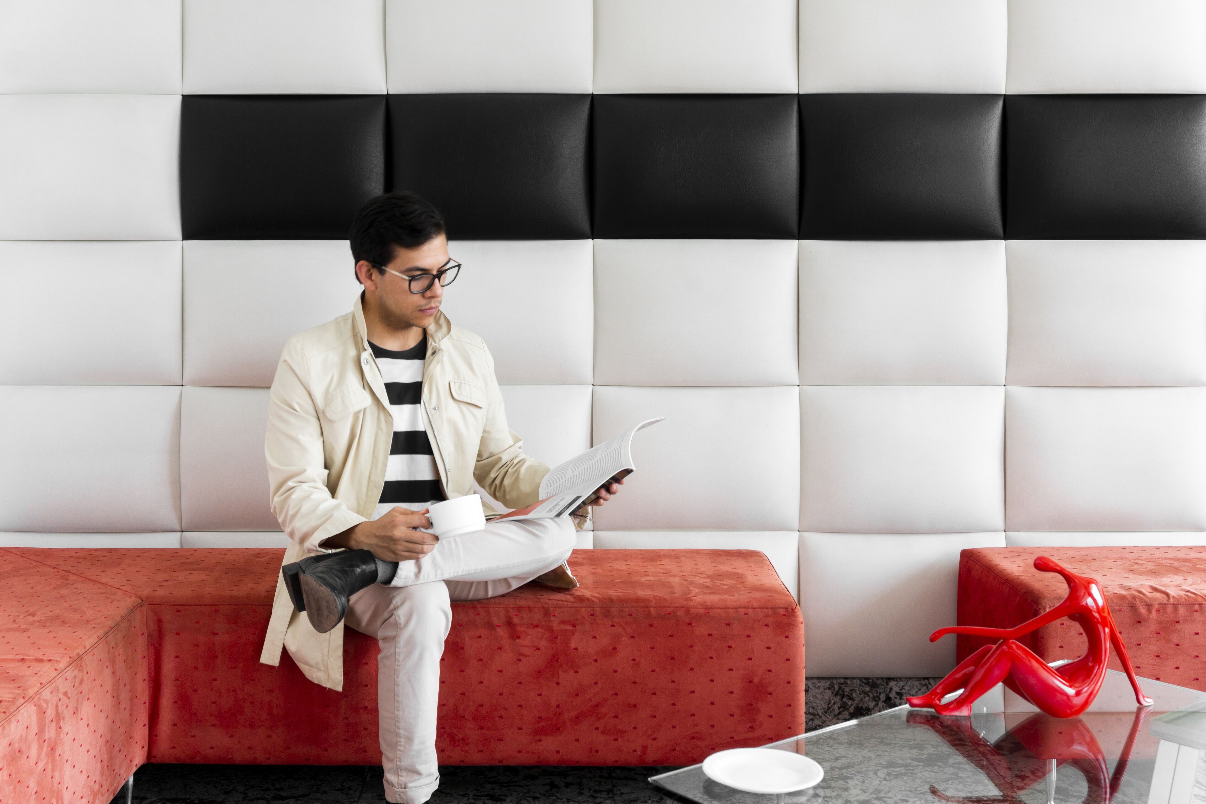 A person sitting on a red sofa in a room with a white and black padded headboard.