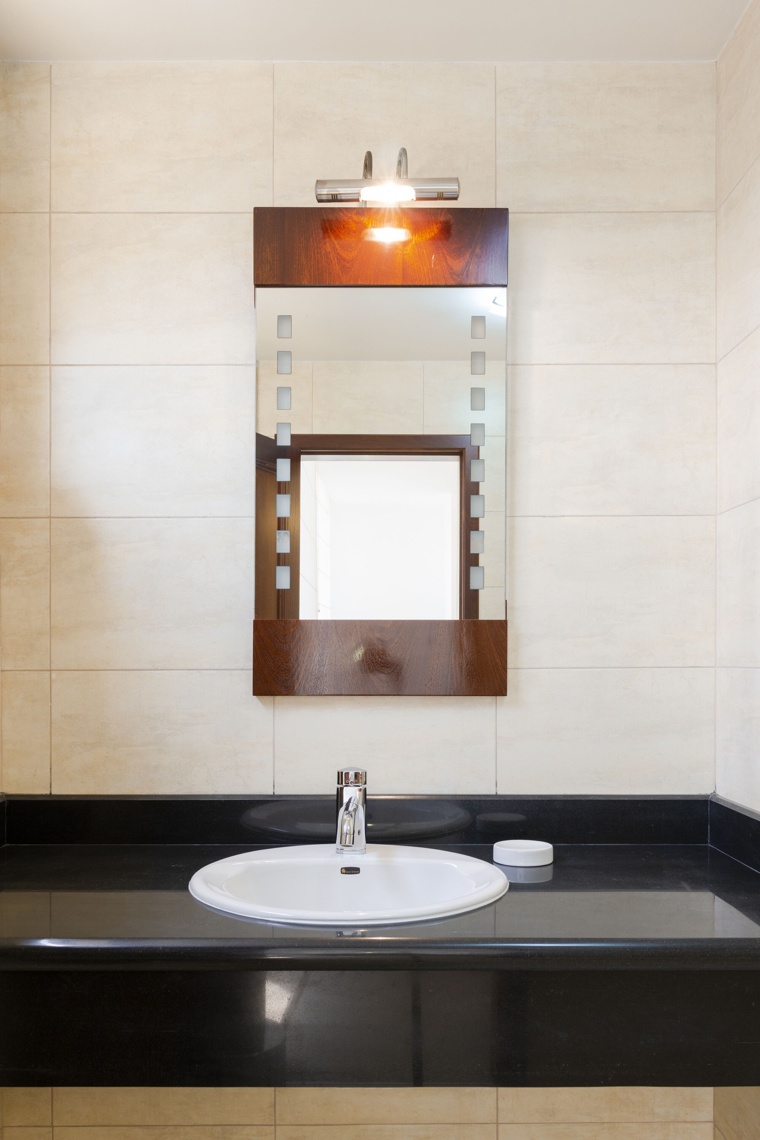 Een badkamer met een wit wastafel, een spiegel met houten lijst, en een zwart aanrecht.