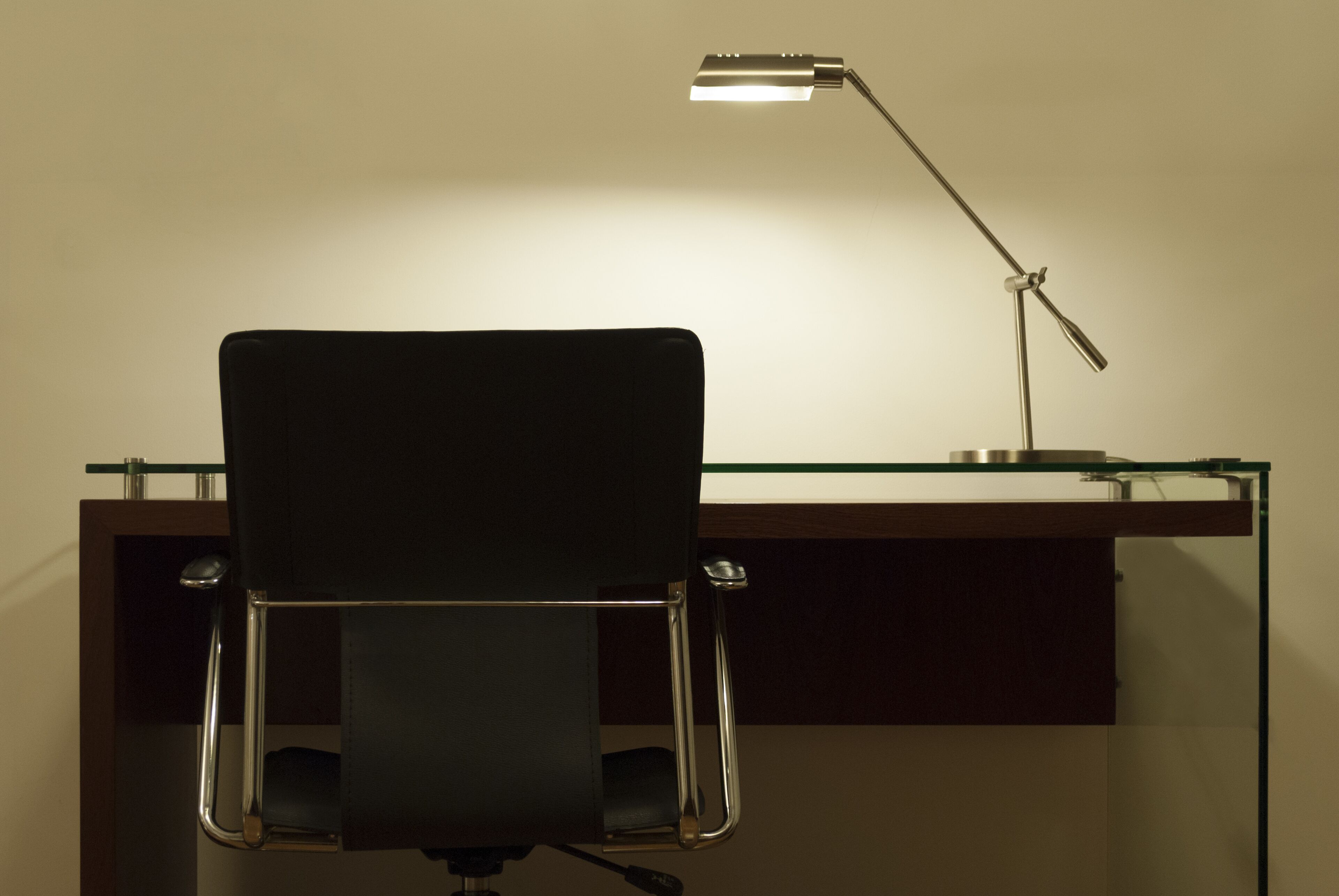 Een bureau met een stoel, een lamp en een glazen blad.
