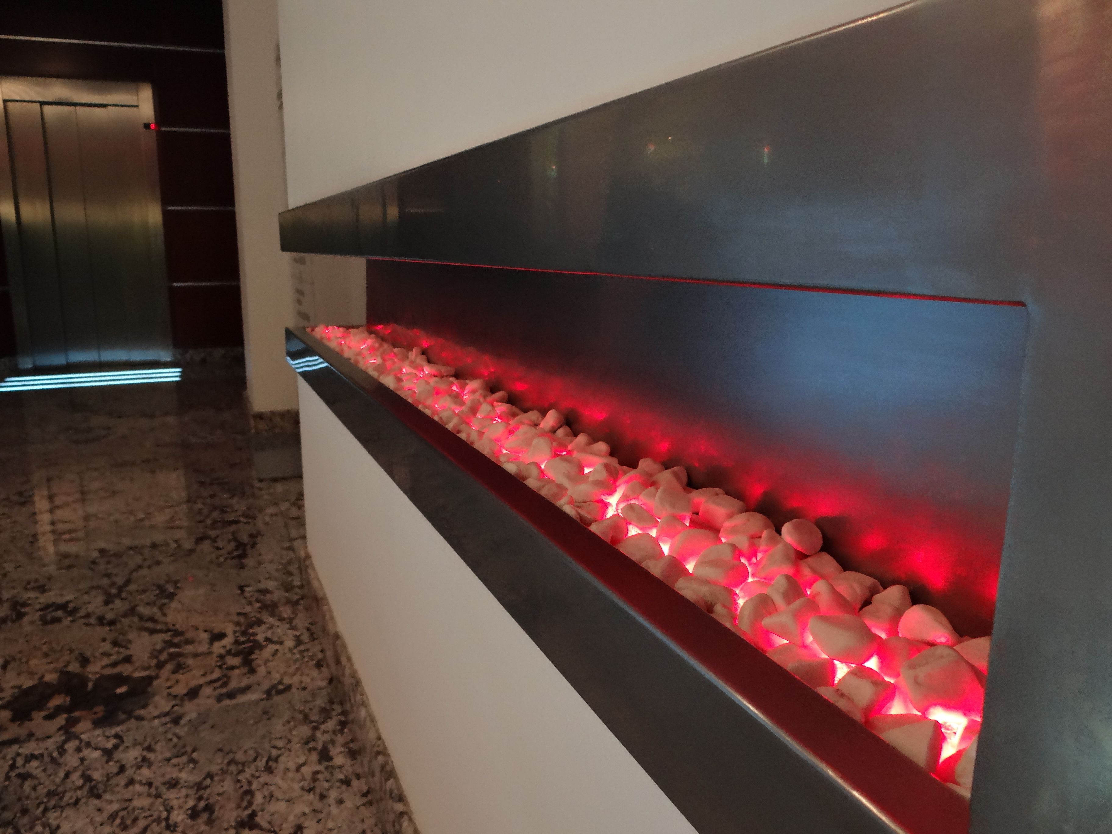 A modern reception area with a marble floor, a reception desk, and a red-lit water feature.