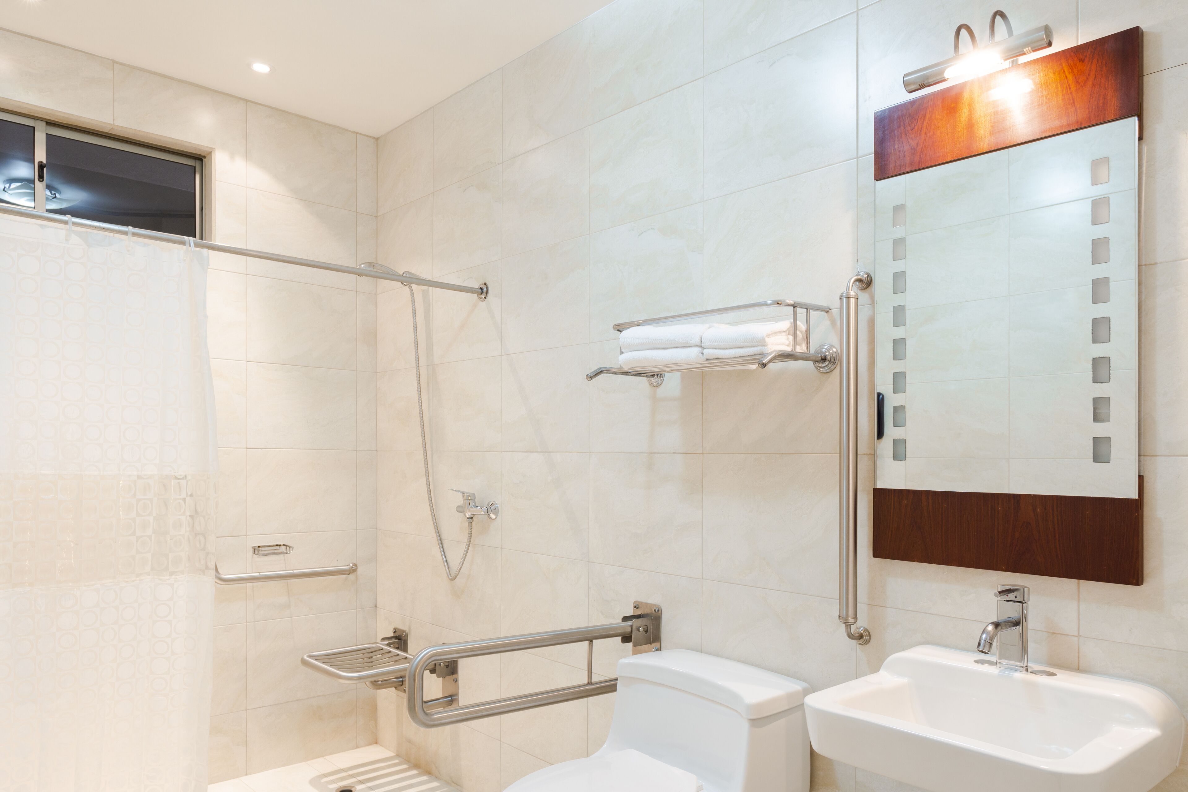 A bathroom with a shower, toilet, and sink, equipped with grab bars and a towel rack.